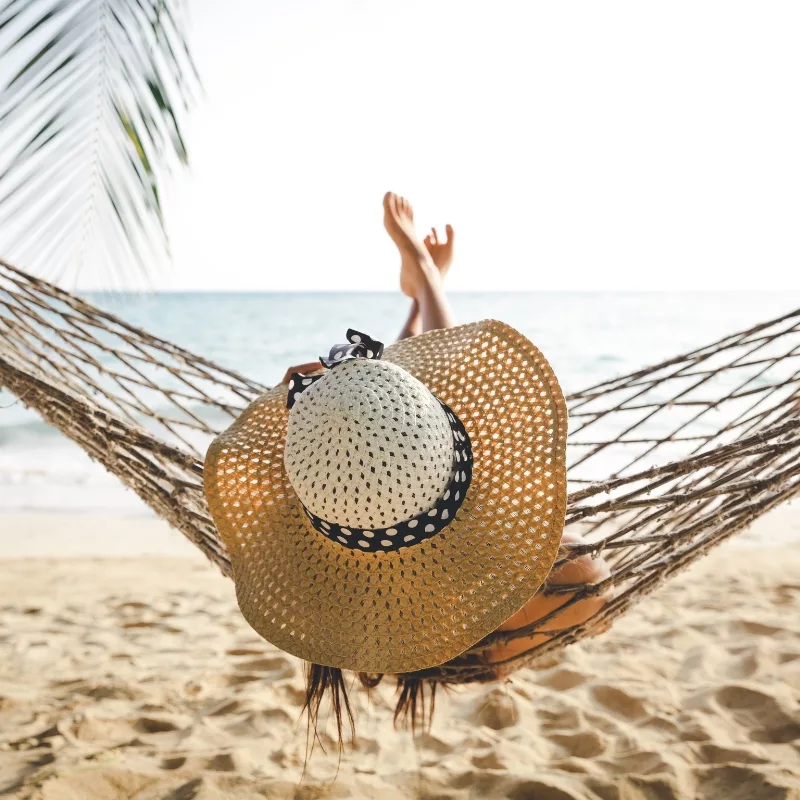 Woman in a sun hat relaxing in a hammock on the beach