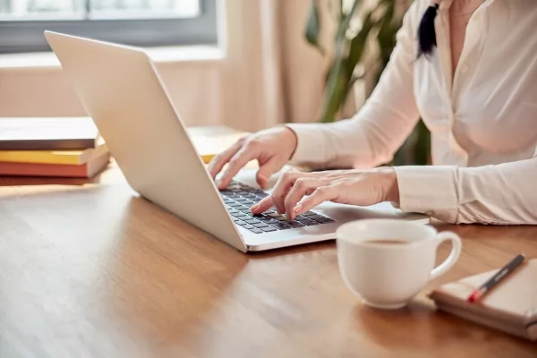 Woman typing on a laptop beside a cup of coffee